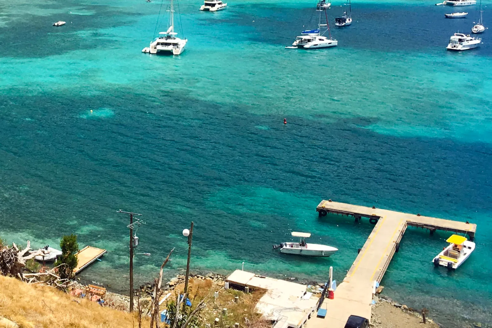 Small boats tied up at the quiet dock in Great Harbour, Jost Van Dyke, with clear turquoise water and anchored yachts beyond