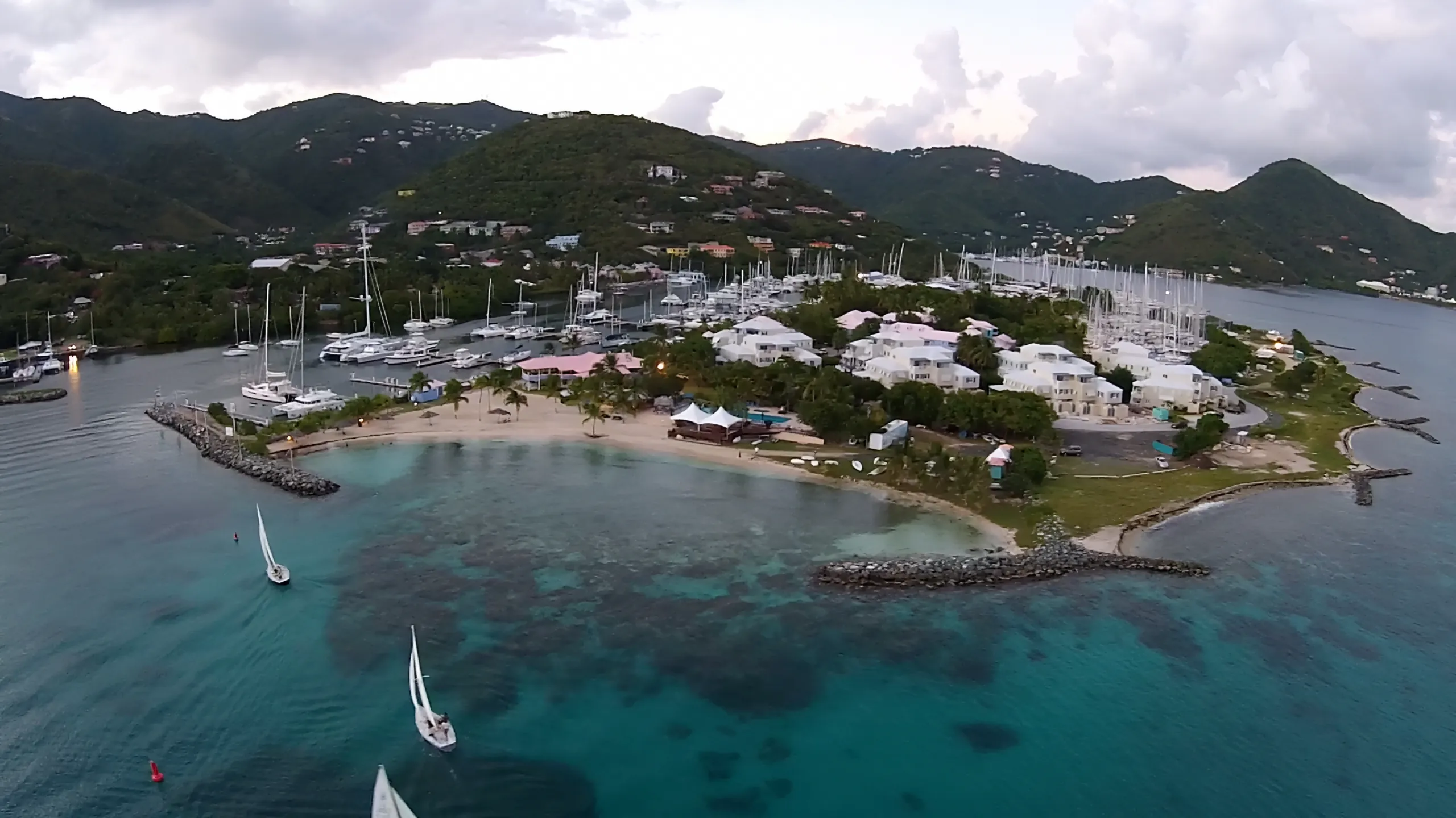 Aerial view of Nanny Cay on Tortola's south coast: marina, beach and sailboats on the water, with green hills rising behind
